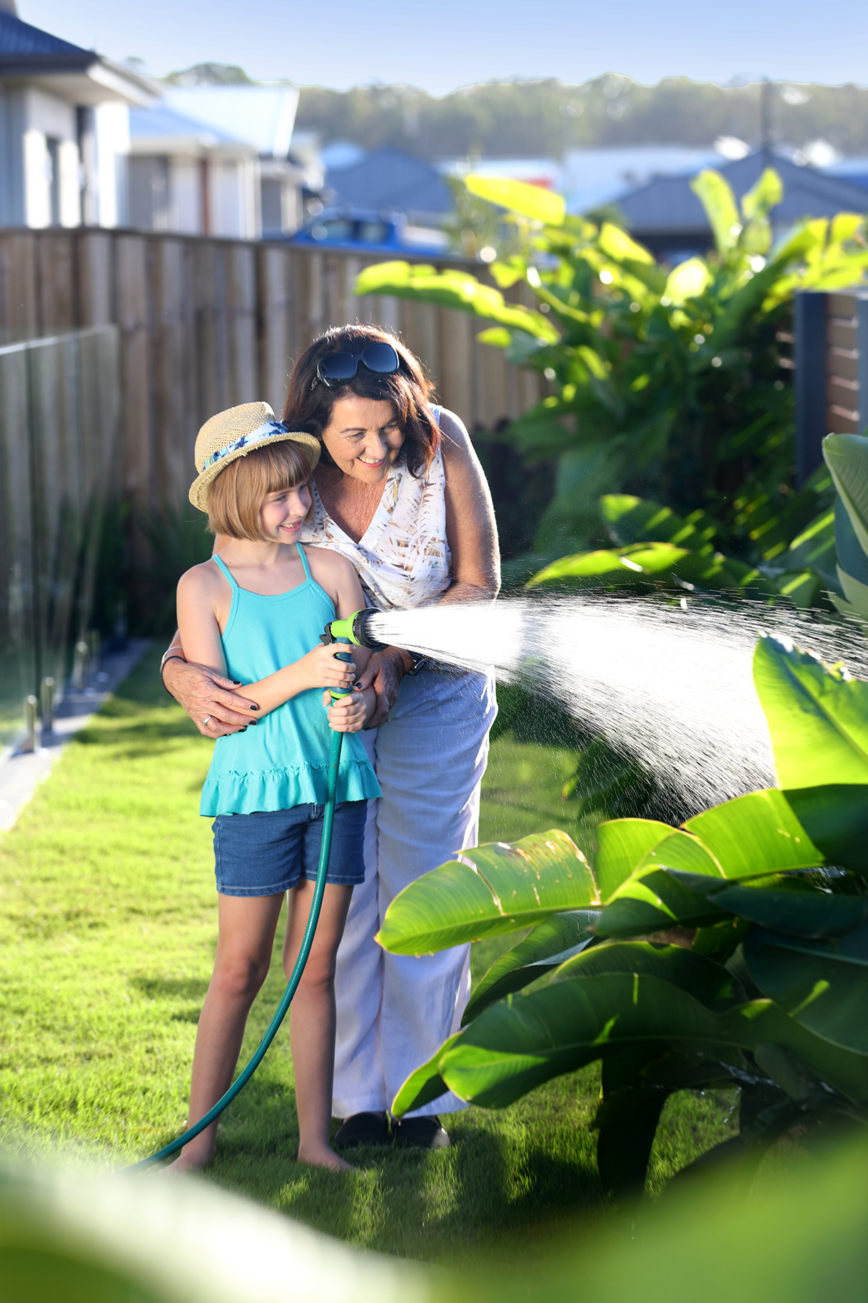 Woman and girl watering residential garden with hose