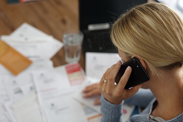 Woman calling on mobile phone while sitting at desk covered with bills