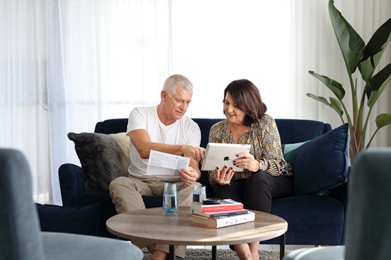 Man and woman sitting on couch looking at Unitywater bill and iPad