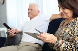 Man holding TV remote woman looking at tablet with credit card on couch
