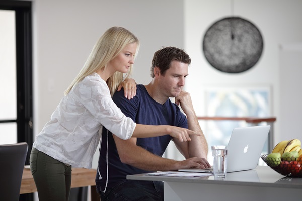 Woman and man looking at laptop computer on residential kitchen bench