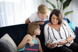 Woman sitting on couch with young girl and boy looking at tablet