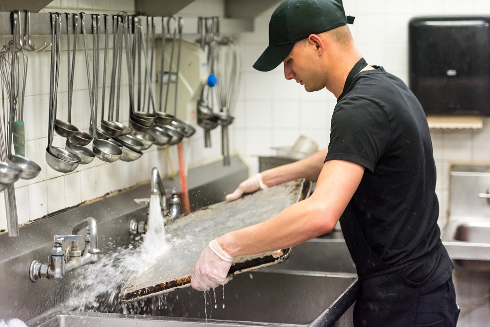 Man washing cooking tray in commercial kitchen
