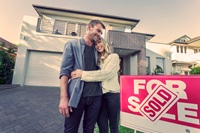 Couple standing in front of a new home with Sold sign