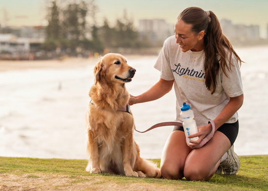 Cara Koenen patting her dog with her reusable water bottle at the beach