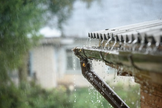 Rain falling on house roof with overflowing gutter