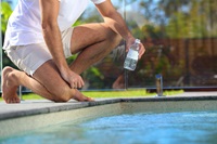 Man filling water testing bottle with water from swimming pool