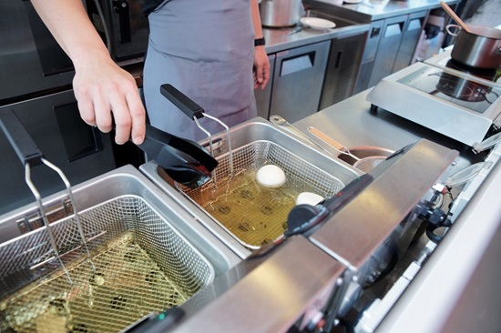 Chef cooking with deep fryer in commercial kitchen