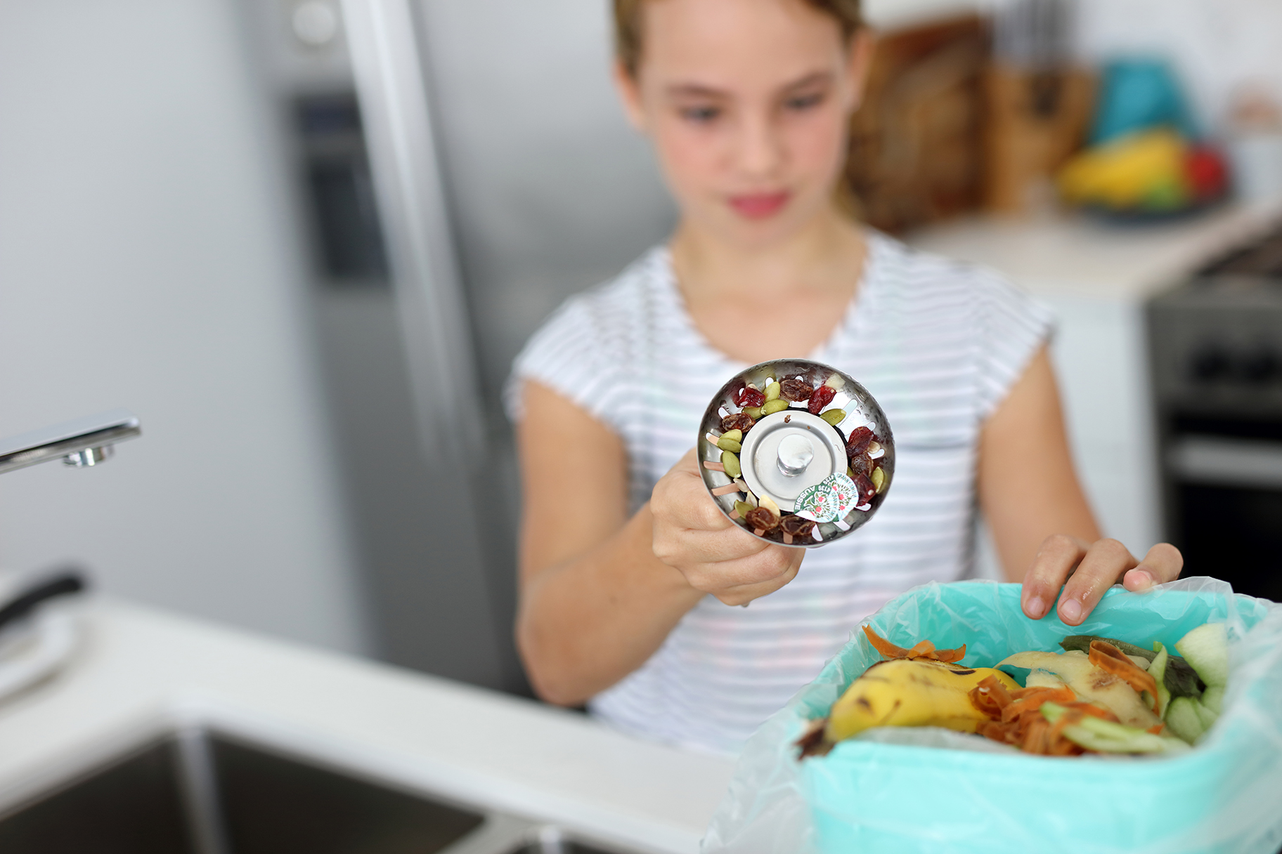 Girl emptying sink strainer full of food scraps into bin on kitchen bench