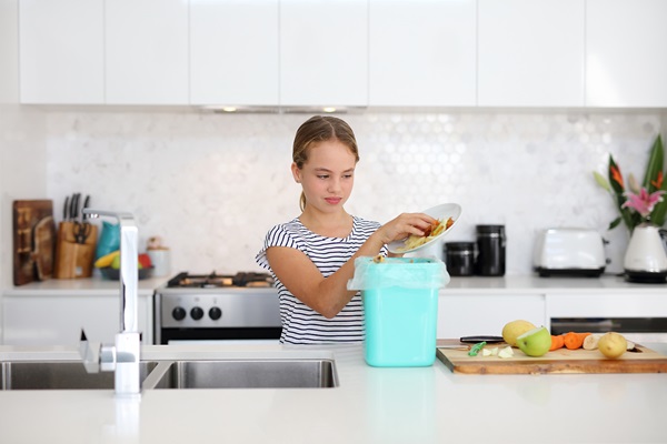 Girl putting food scraps from a plate into the compost bin on kitchen bench