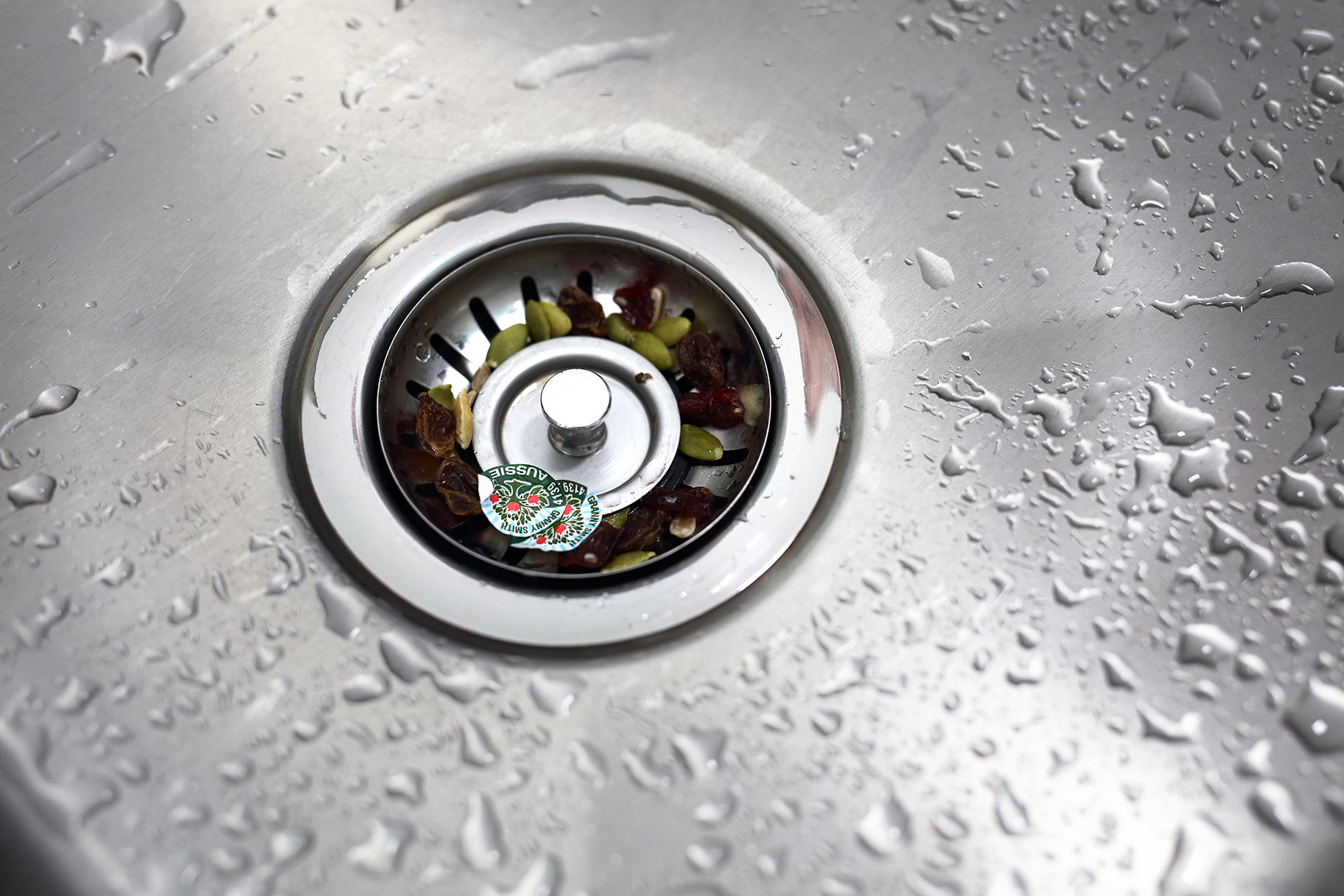 Kitchen sink strainer full of food scraps and fruit stickers