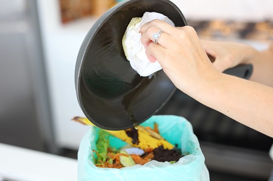 Woman wiping oil from frypan into bin on kitchen bench
