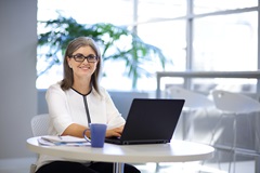 Female staff member typing on laptop computer with coffee in office