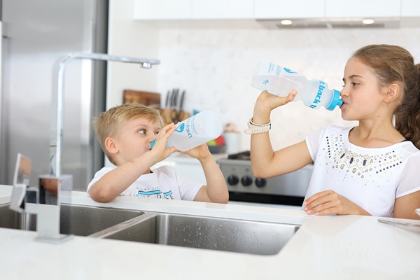 Children drinking from water bottles at kitchen sink