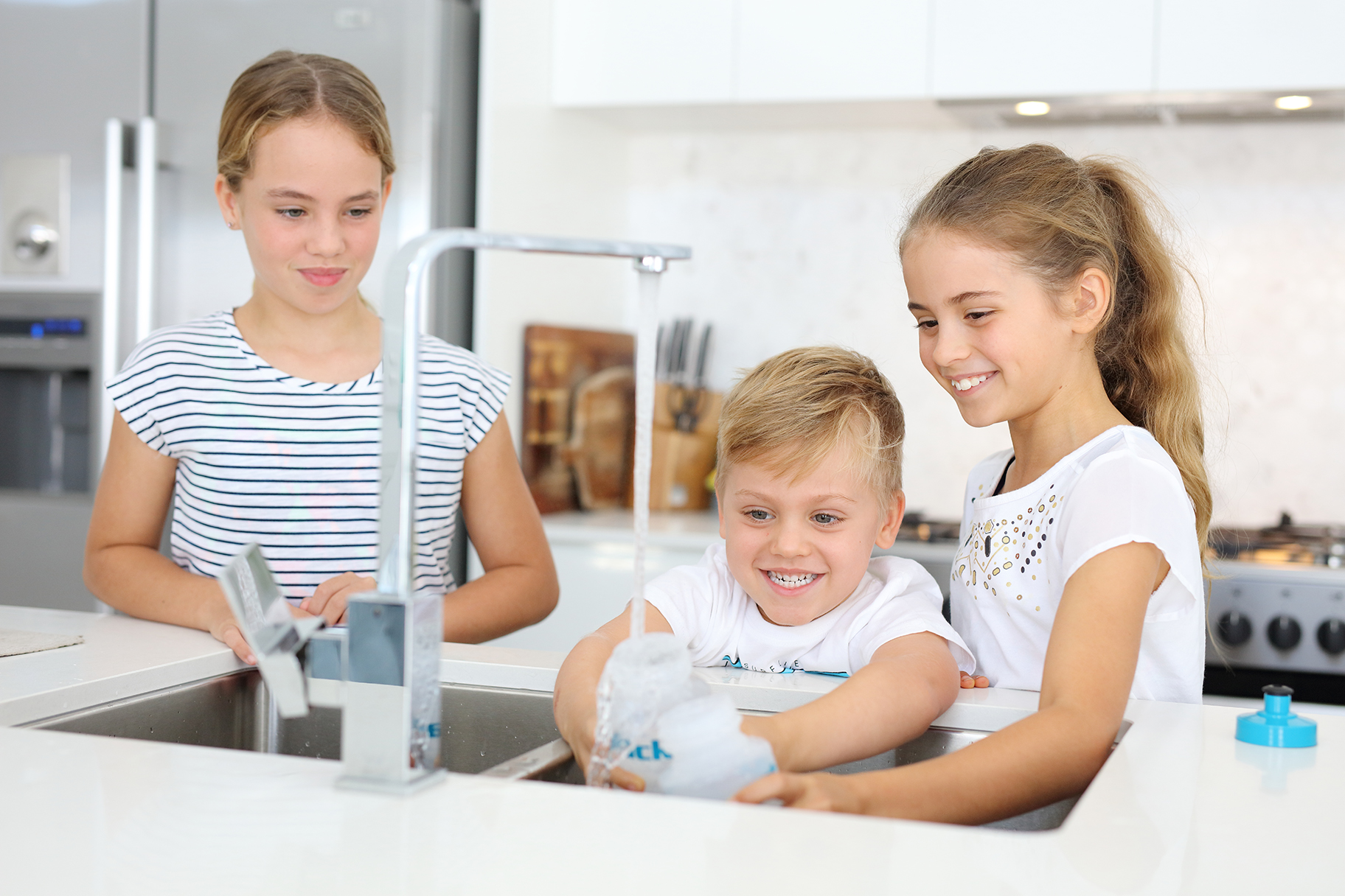 Children filling water bottles at kitchen sink