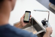 Man looking at phone while checking for water outage at kitchen sink with outages map on screen
