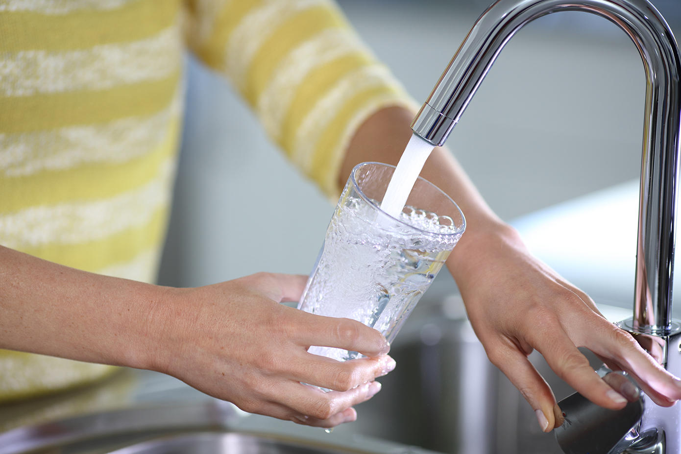 Woman holding glass of bubbly water running out of kitchen tap
