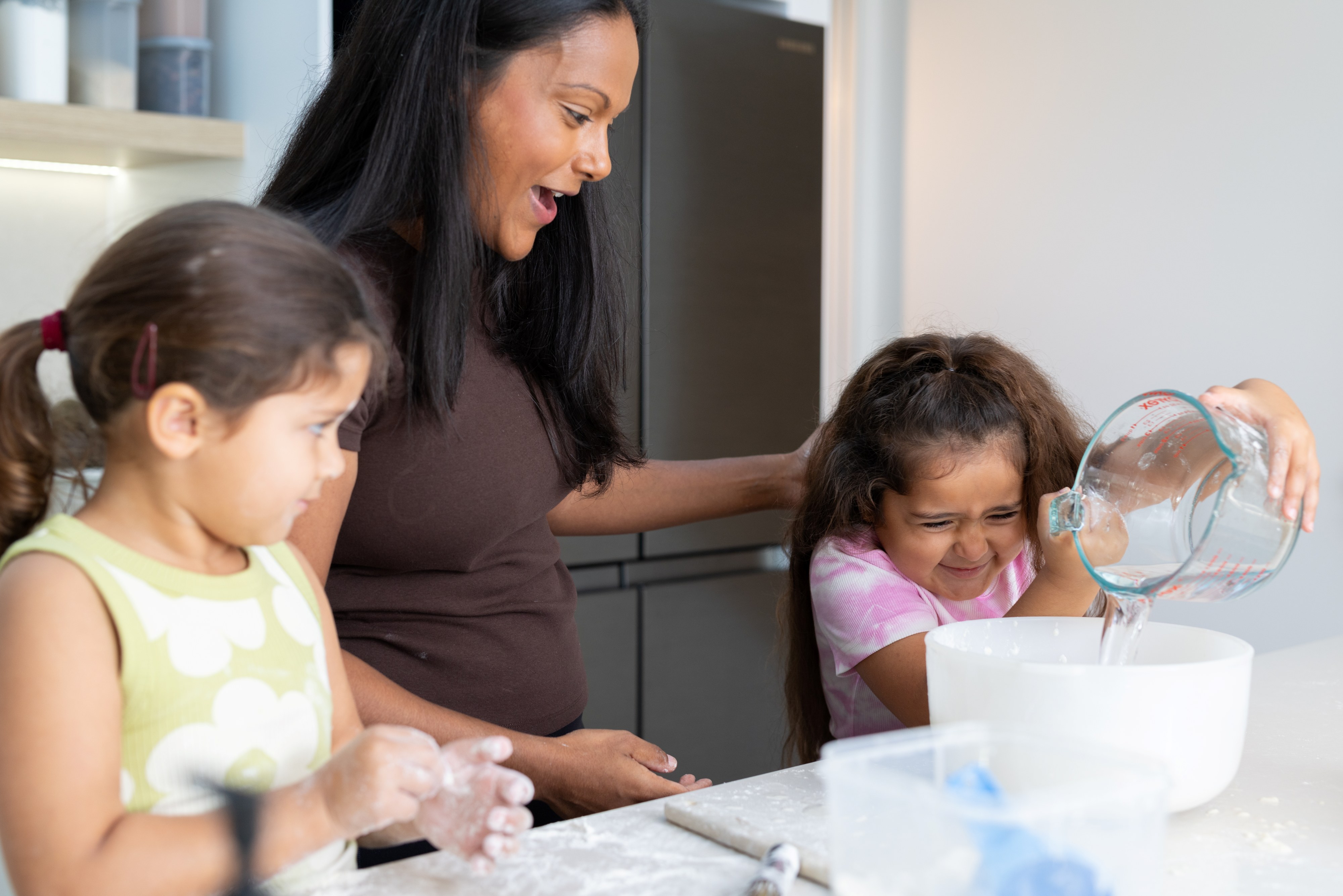 Parent with two children in kitchen pouring water into mixing bowl