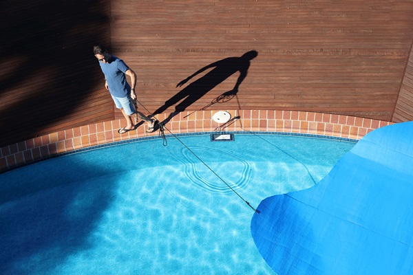 Man covering residential pool with blue tarp