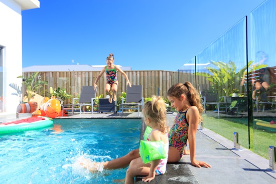 Girls sitting by residential pool and boy jumping in
