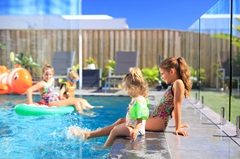 Kids sitting by residential pool and floating on pool toys in the background